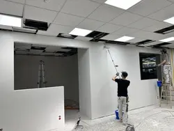 Foto zweier Mitarbeiters der Malerei Norbert Bardtke beim Streichen einer Wand mit weißer Farbe und einer Rolle. Die Wände des Raumes sind mit Plastikfolie behängt. Einer der beiden Männer steht auf einer Leiter, der andere Mann steht auf dem Boden mit einer langen Rolle in der Hand.