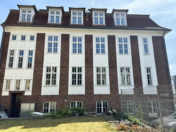 Außenaufnahme eines großen gemauerten Hauses mit Betonfassade-Elementen. Die Betonfassade ist in einem hellen Farbton von der Malerei Norbert Bardtke gestrichen.